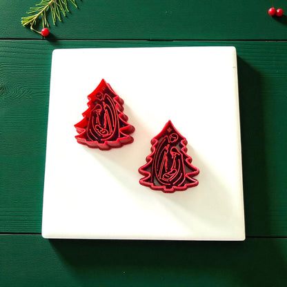 Pair of red nativity tree cutters on white tile with Christmas greenery