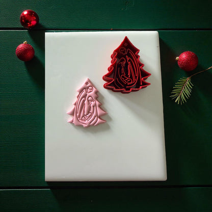 Pink clay imprint beside red nativity tree cutter on white tile and green background
