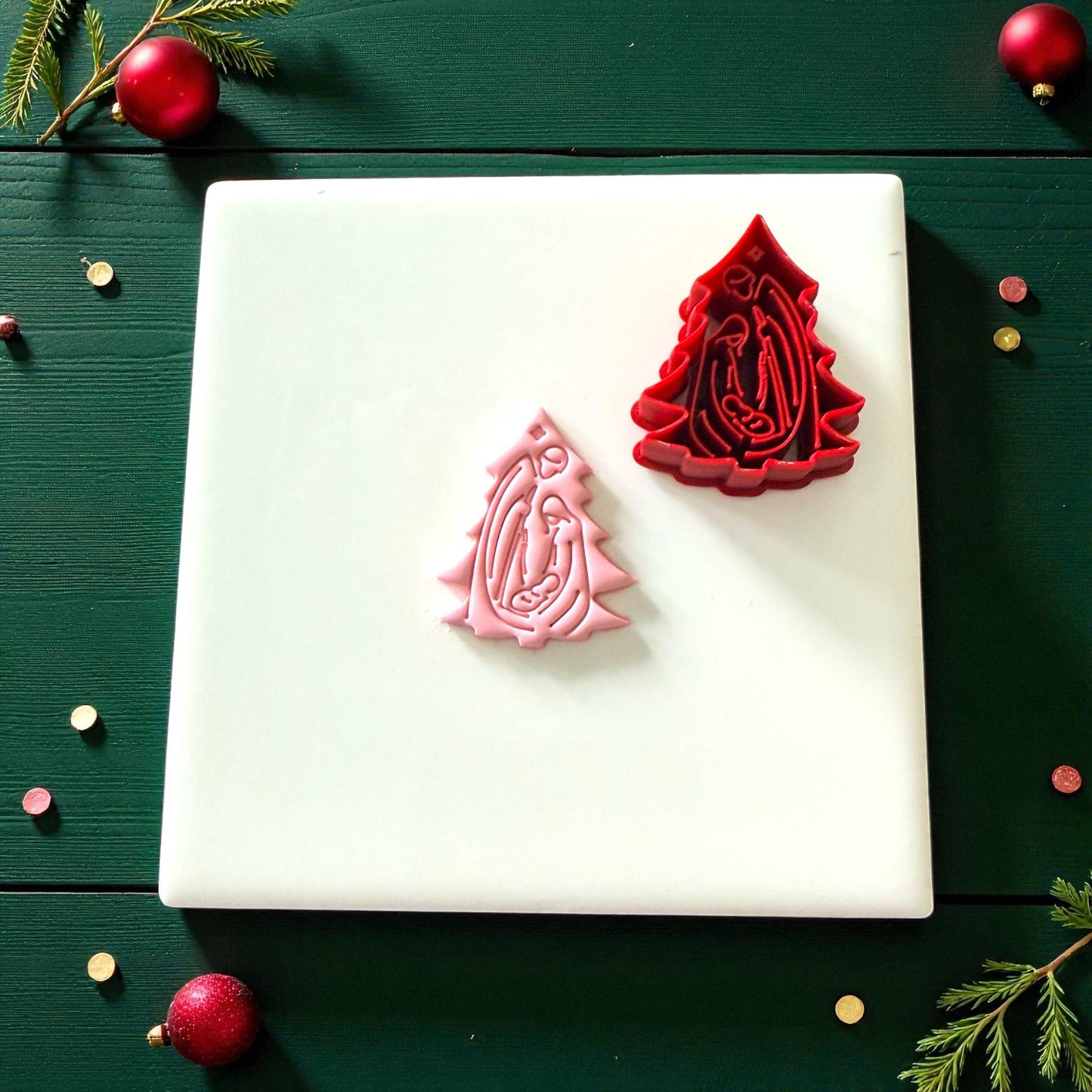 Pink clay imprint and red nativity tree cutter on white tile with ornaments