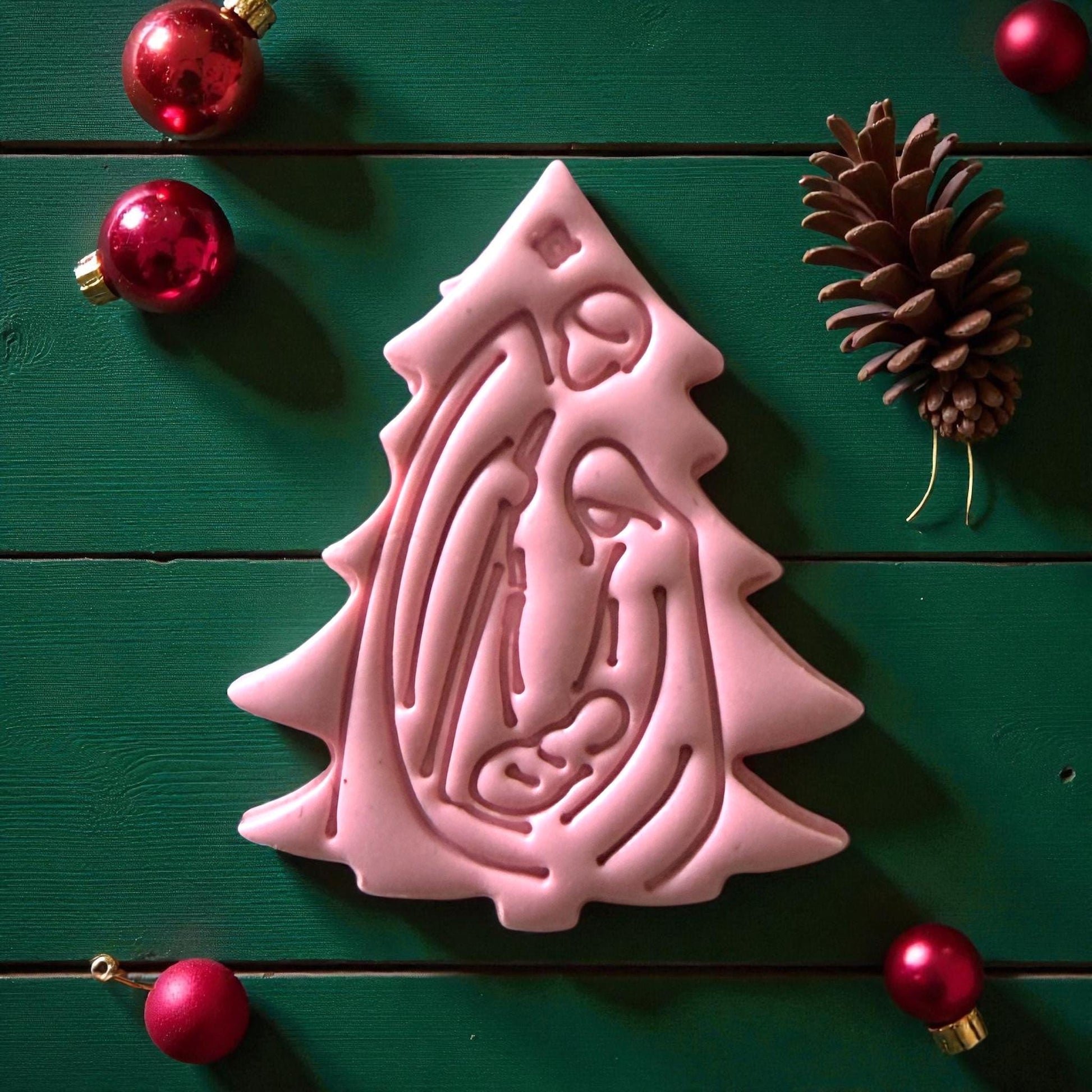 Pink nativity tree clay imprint surrounded by red ornaments and pinecone