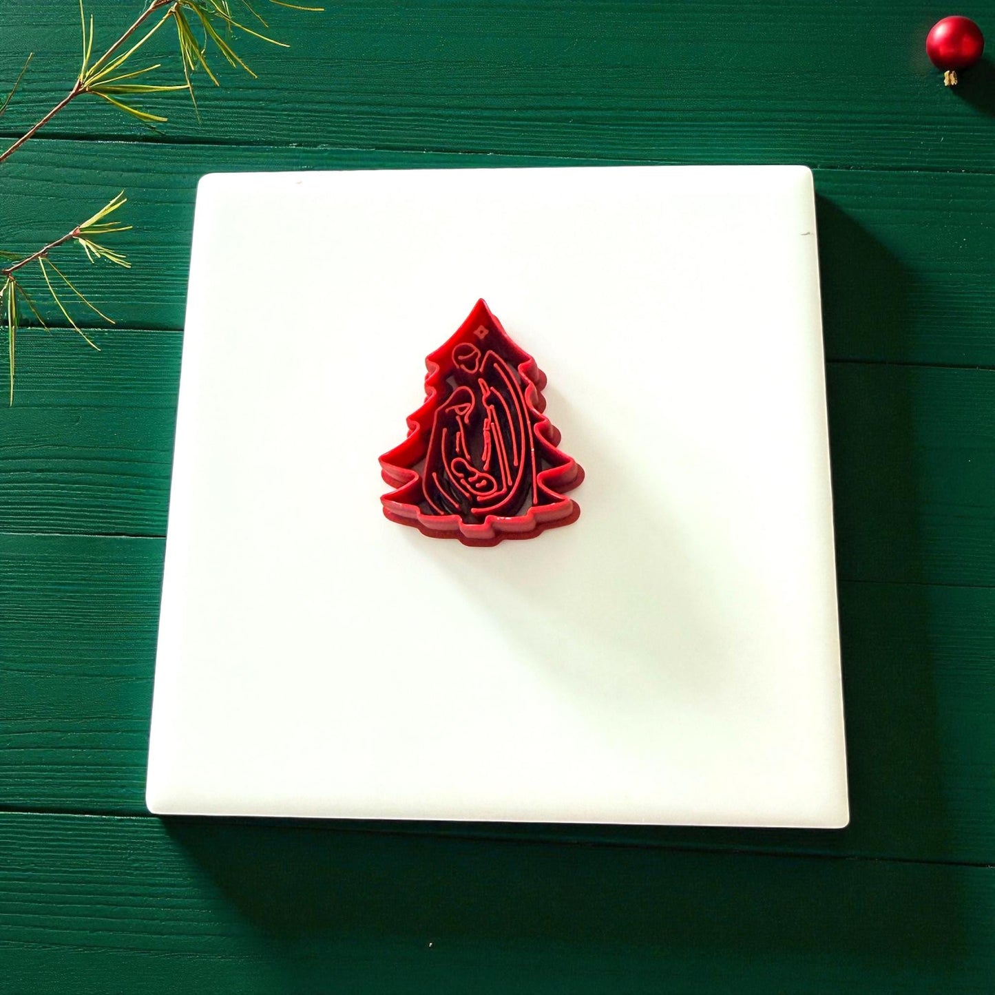 Red nativity tree polymer clay cutter on white tile with holiday decor