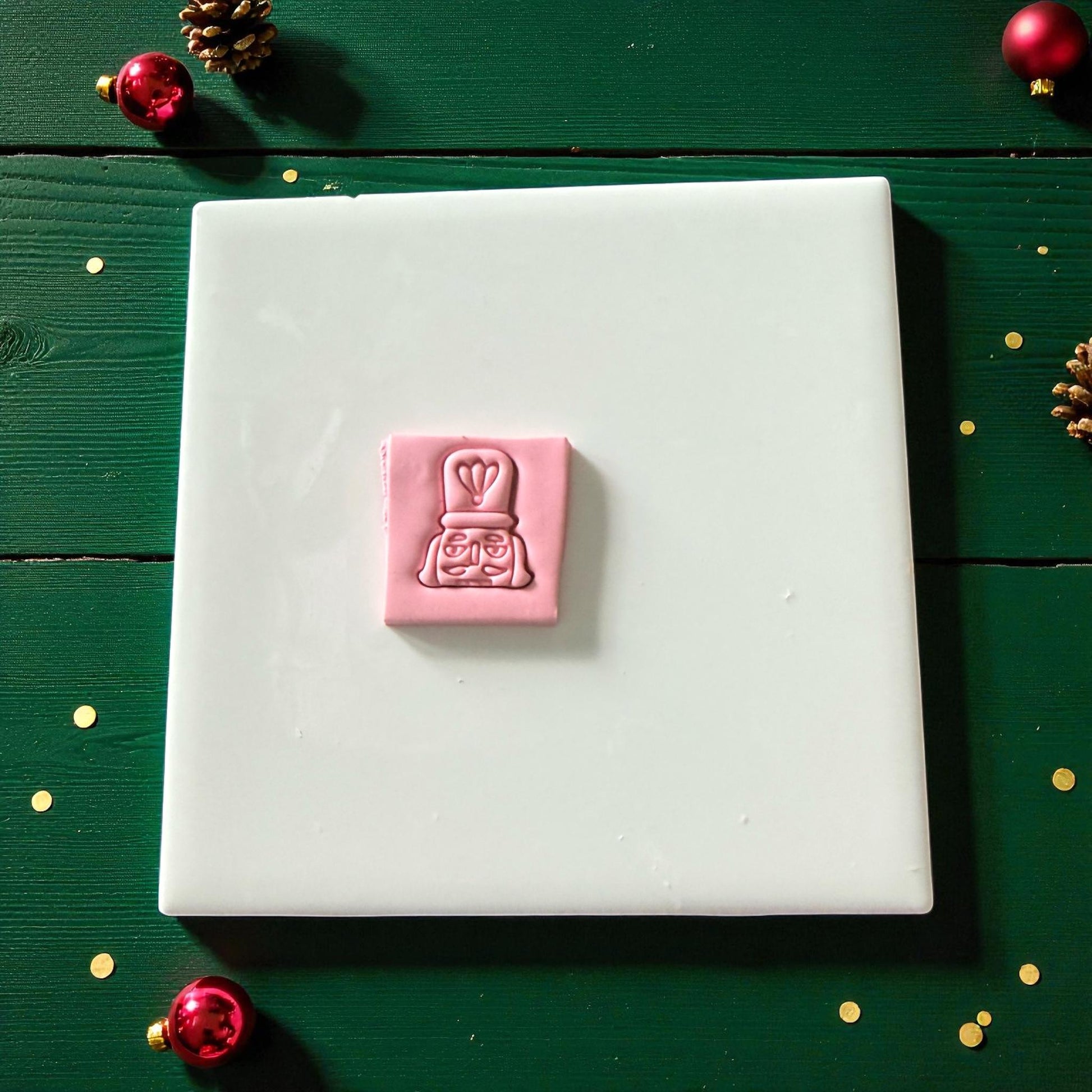 Pink nutcracker imprint pressed into square clay sheet on white tile