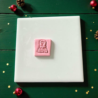 Pink nutcracker imprint pressed into square clay sheet on white tile