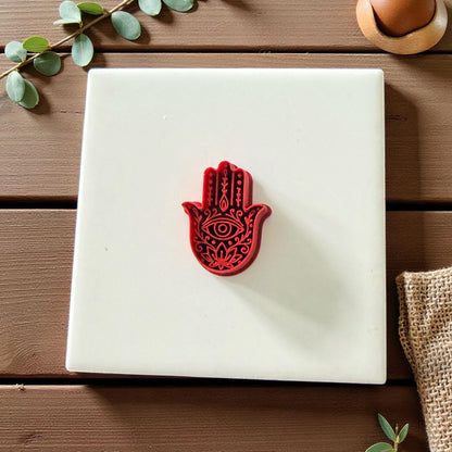 Red Hamsa Hand clay cutter centered on white tile with eucalyptus leaves