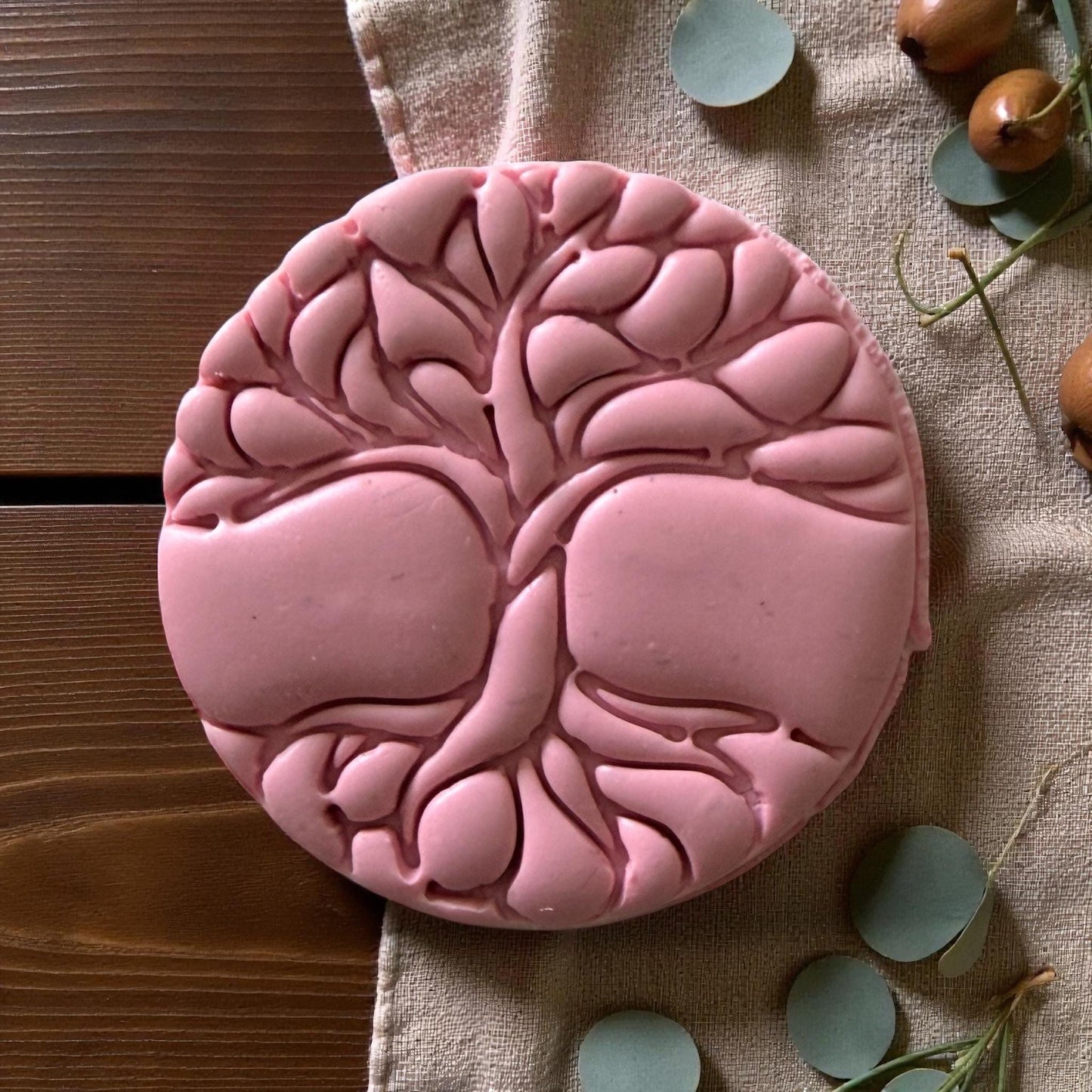 Close-up of pink clay circle embossed with detailed tree of life design