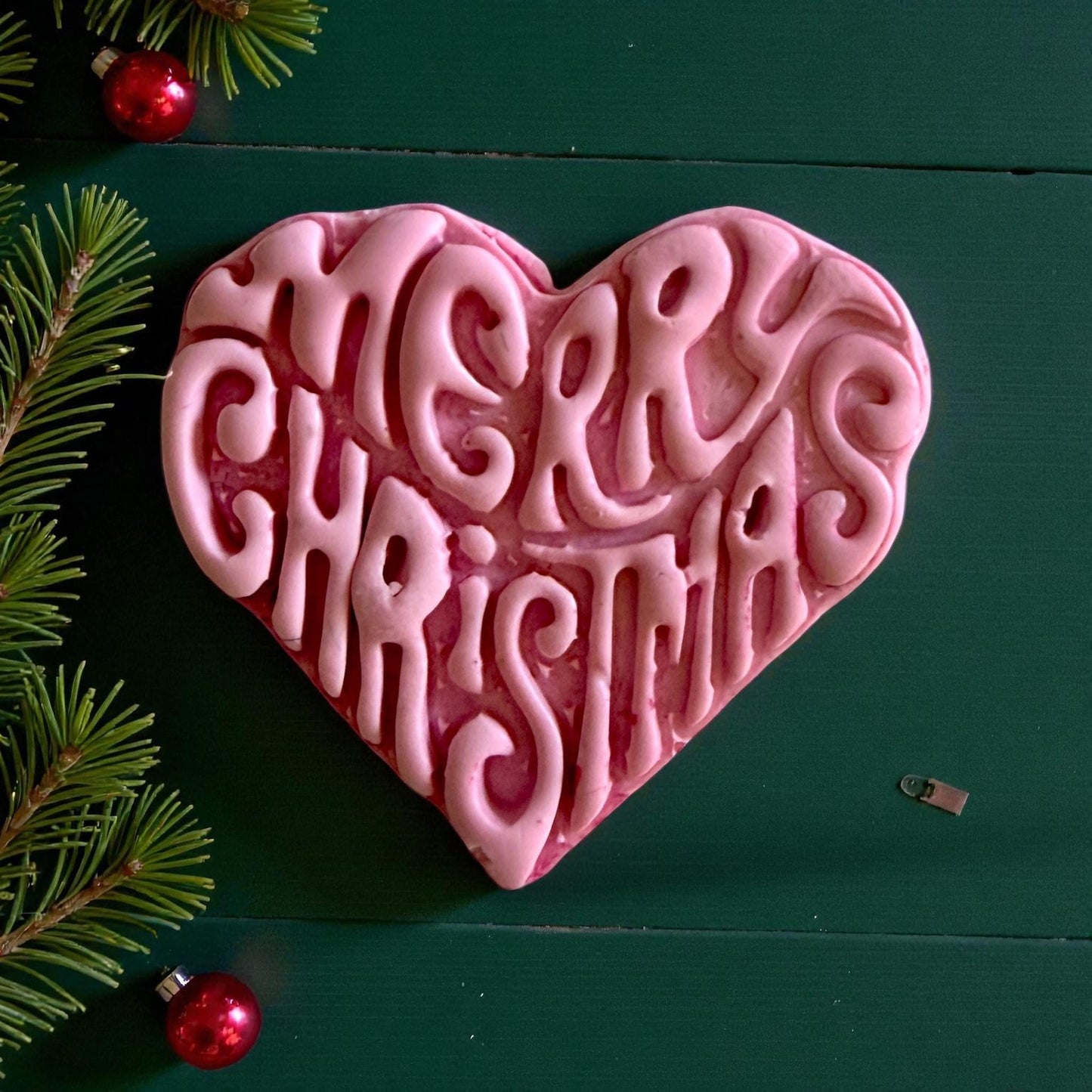 Close-up of pink Merry Christmas heart clay design with pine decor