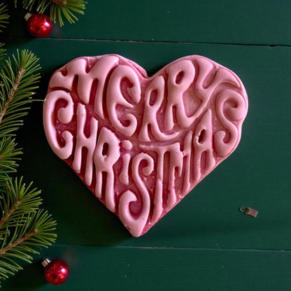 Close-up of pink Merry Christmas heart clay design with pine decor