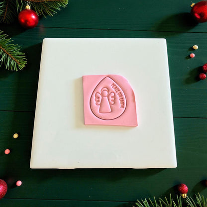 Pink clay square with angel and peace on earth design on white tile