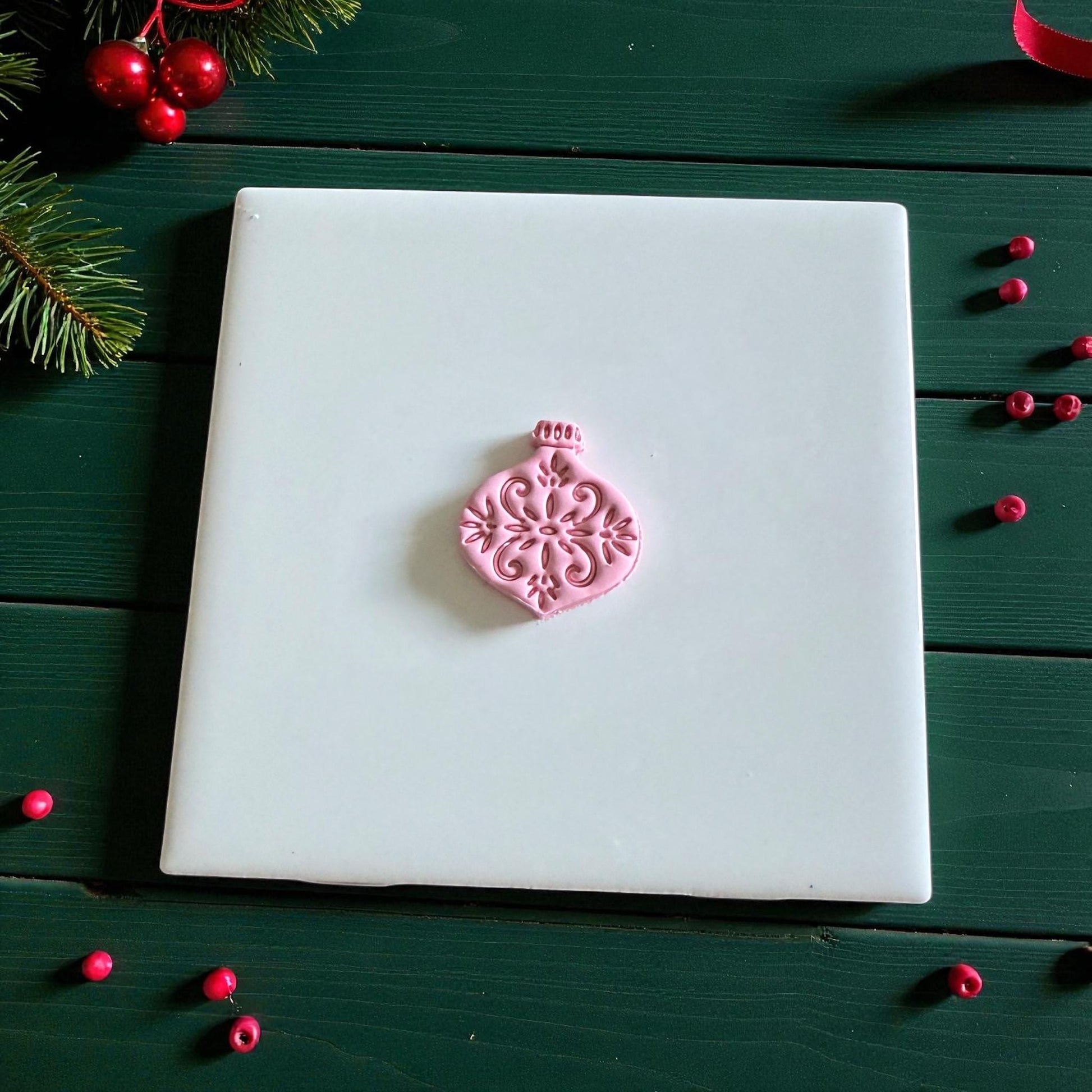 Pink ornament-shaped clay piece on white tile with holiday beads