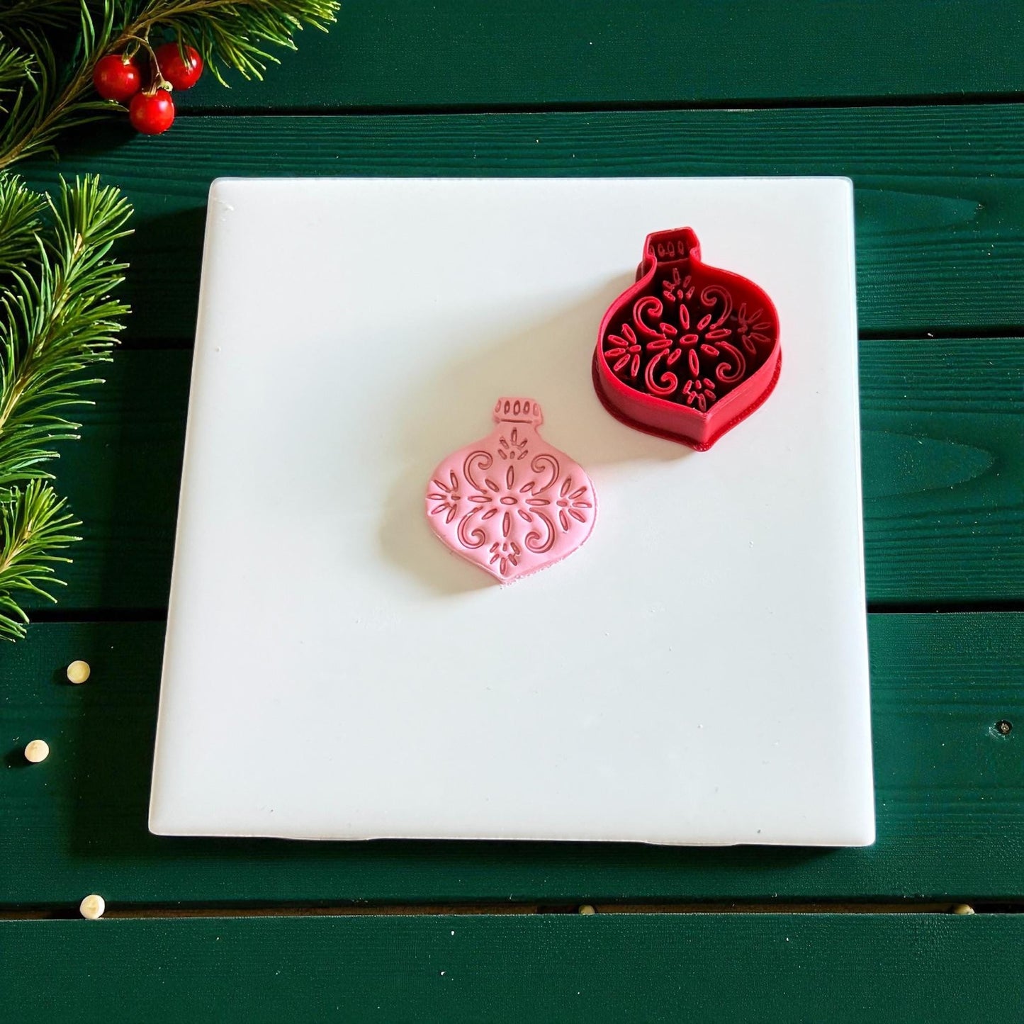 Red cutter and pink ornament clay piece side by side on white tile