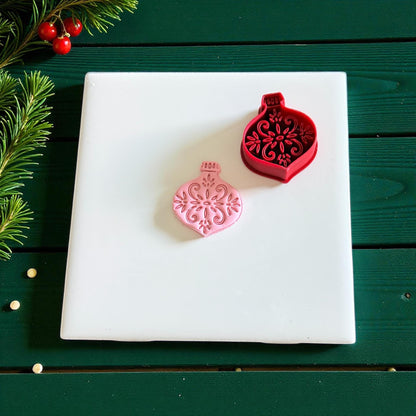Red cutter and pink ornament clay piece side by side on white tile