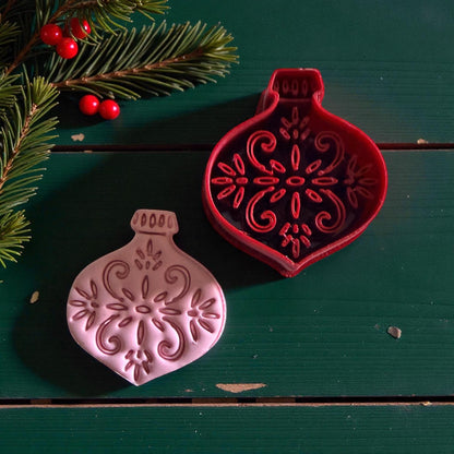 Red ornament cutter and pink clay piece with pine and berries