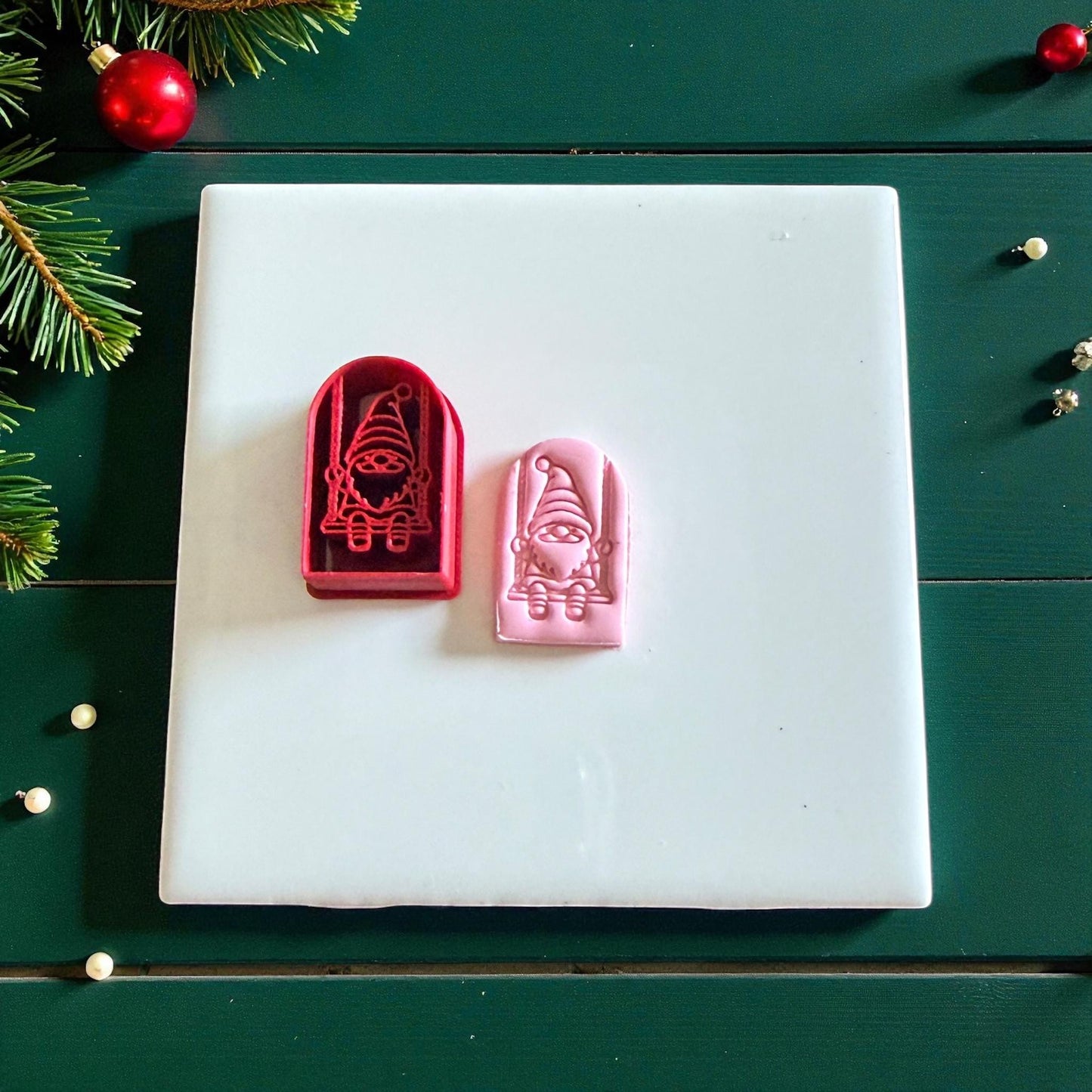 Red cutter and pink gnome clay piece on white tile with pine accents