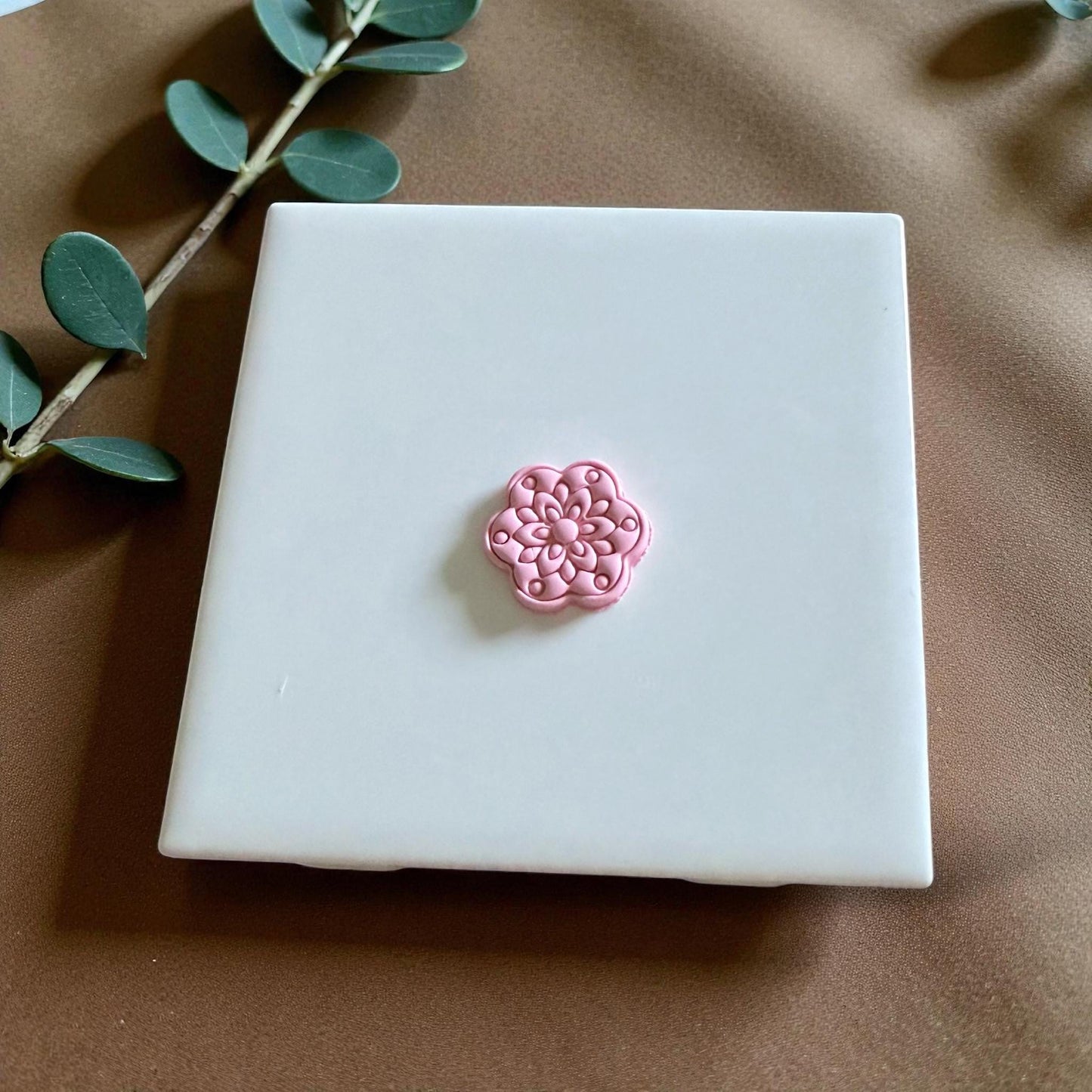 Small pink floral clay piece centered on white tile with leaf stem