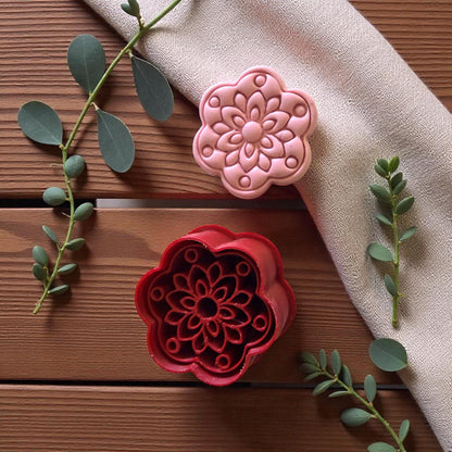 Red cutter and pink floral clay piece on wooden table with greenery