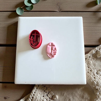 Red cutter and pink clay oval with cross and branch on white tile