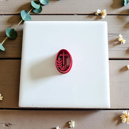 Red oval clay cutter with cross and branch on white tile surrounded by flowers