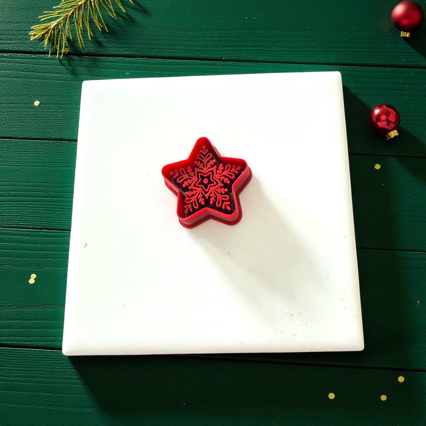 Red star cutter on white tile surrounded by green holiday background and ornaments