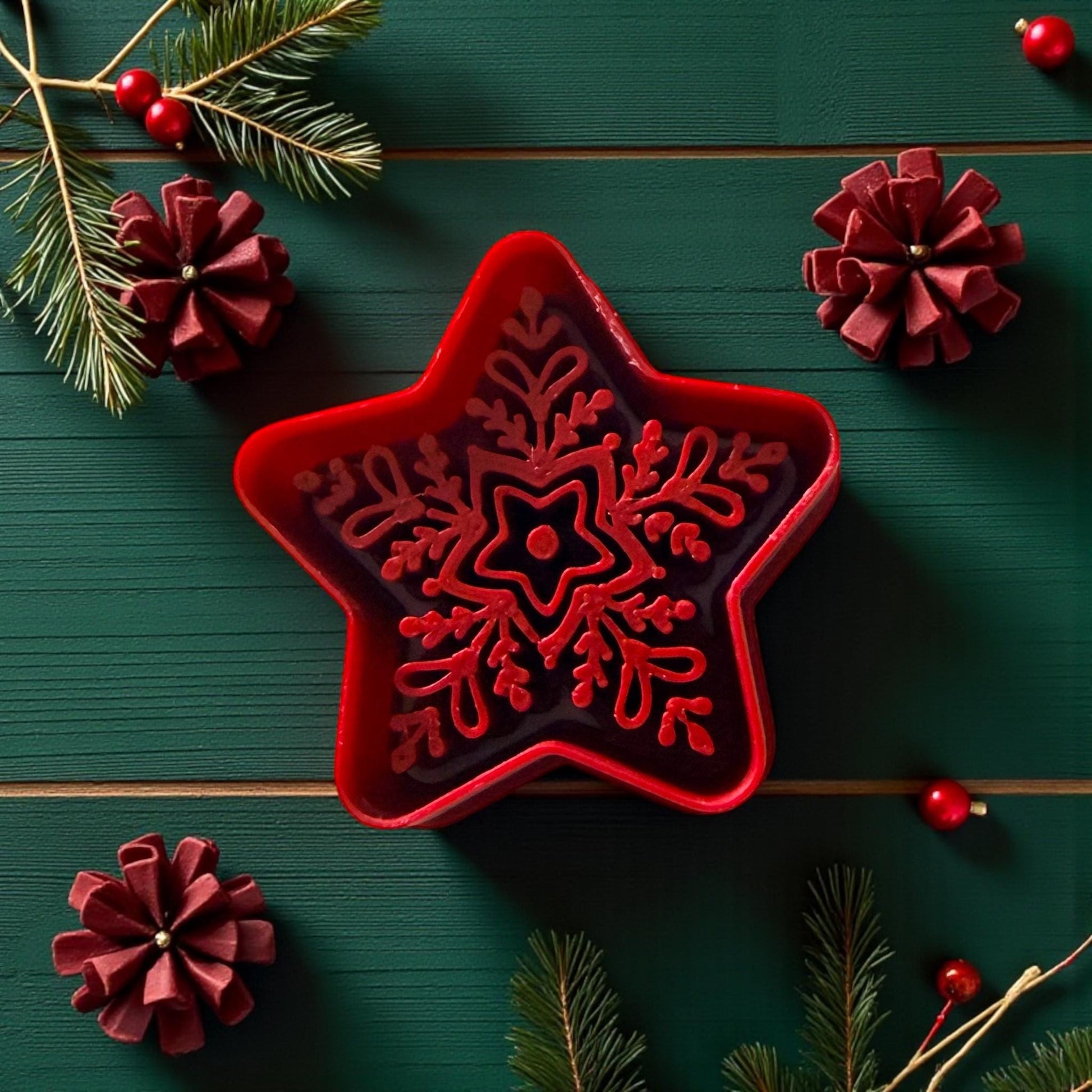 Red star-shaped cutter with snowflake design on green wood background with pine and ribbon