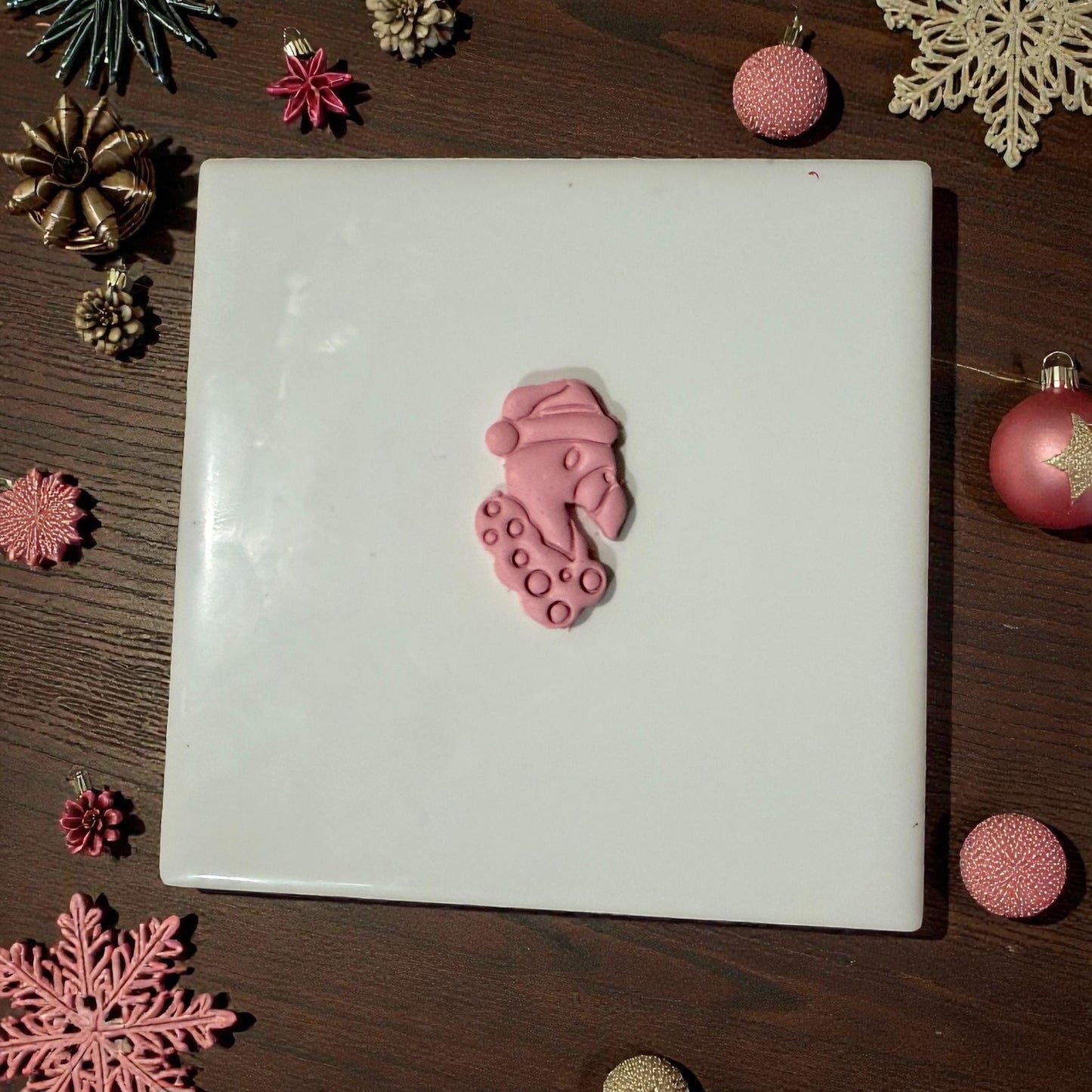 “Flamingo clay piece centered on white tile with holiday decor”