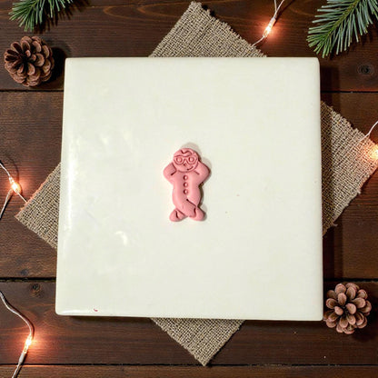 pink snowman clay piece on white tile with pinecones