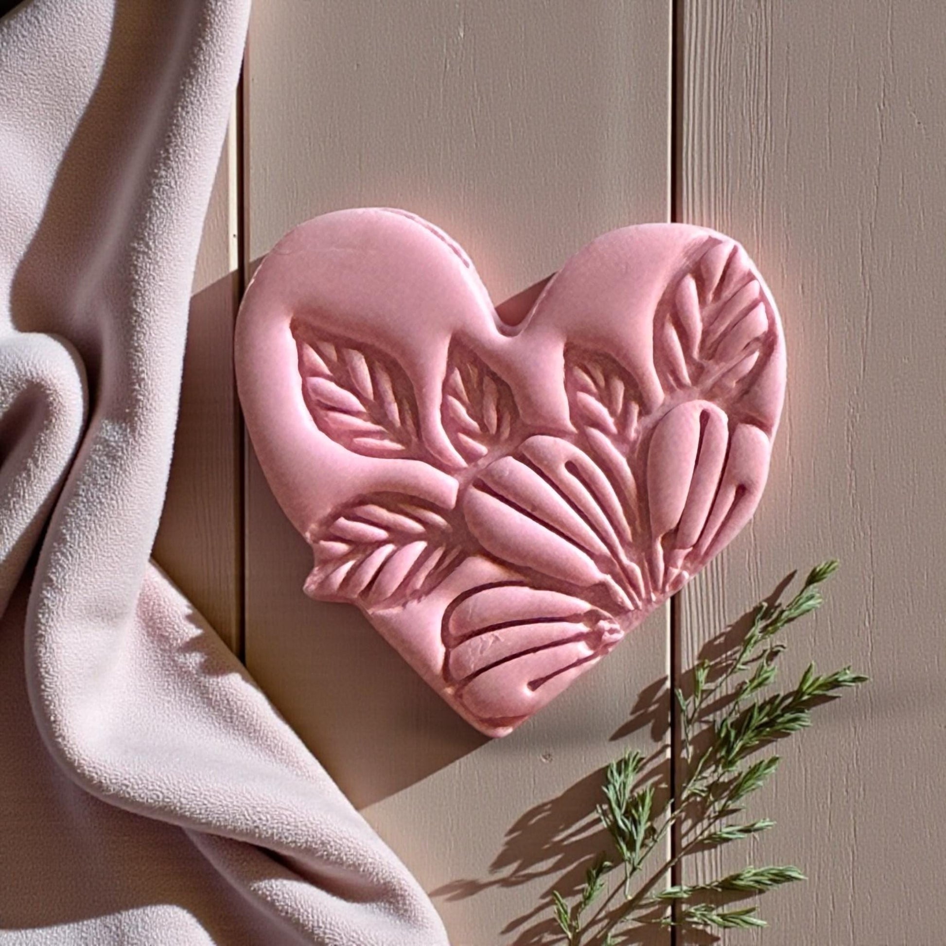 Pink botanical clay heart on wood background with draped fabric and greenery
