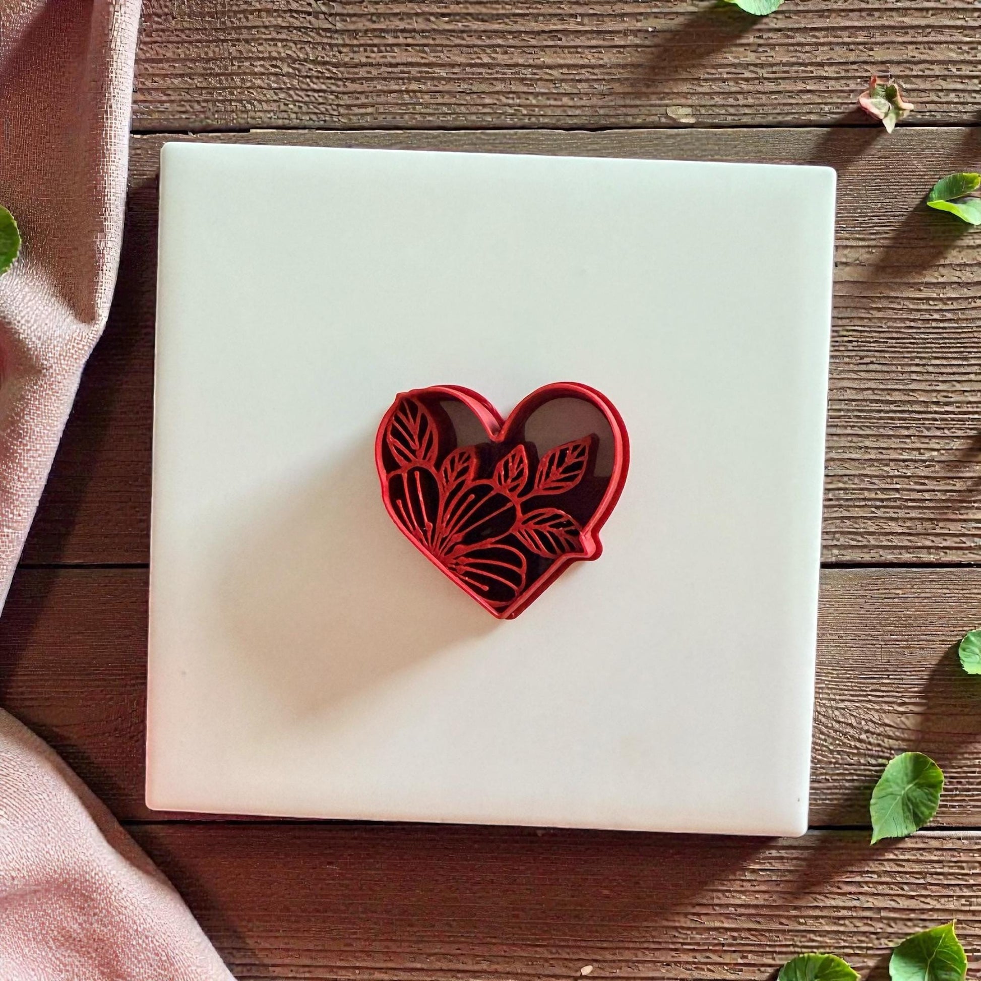 Red floral heart cutter on white tile with soft fabric and wood background