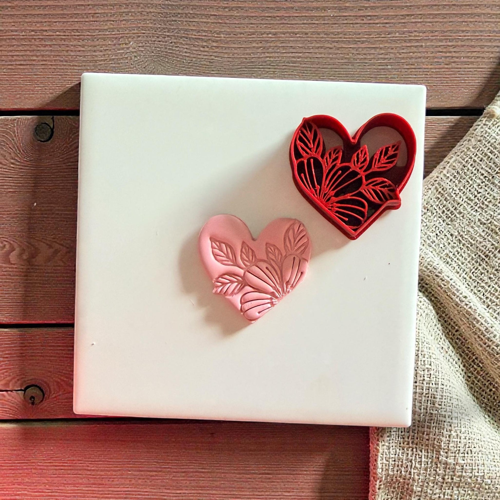 Red heart cutter and pink clay heart impression with leaf pattern on white tile