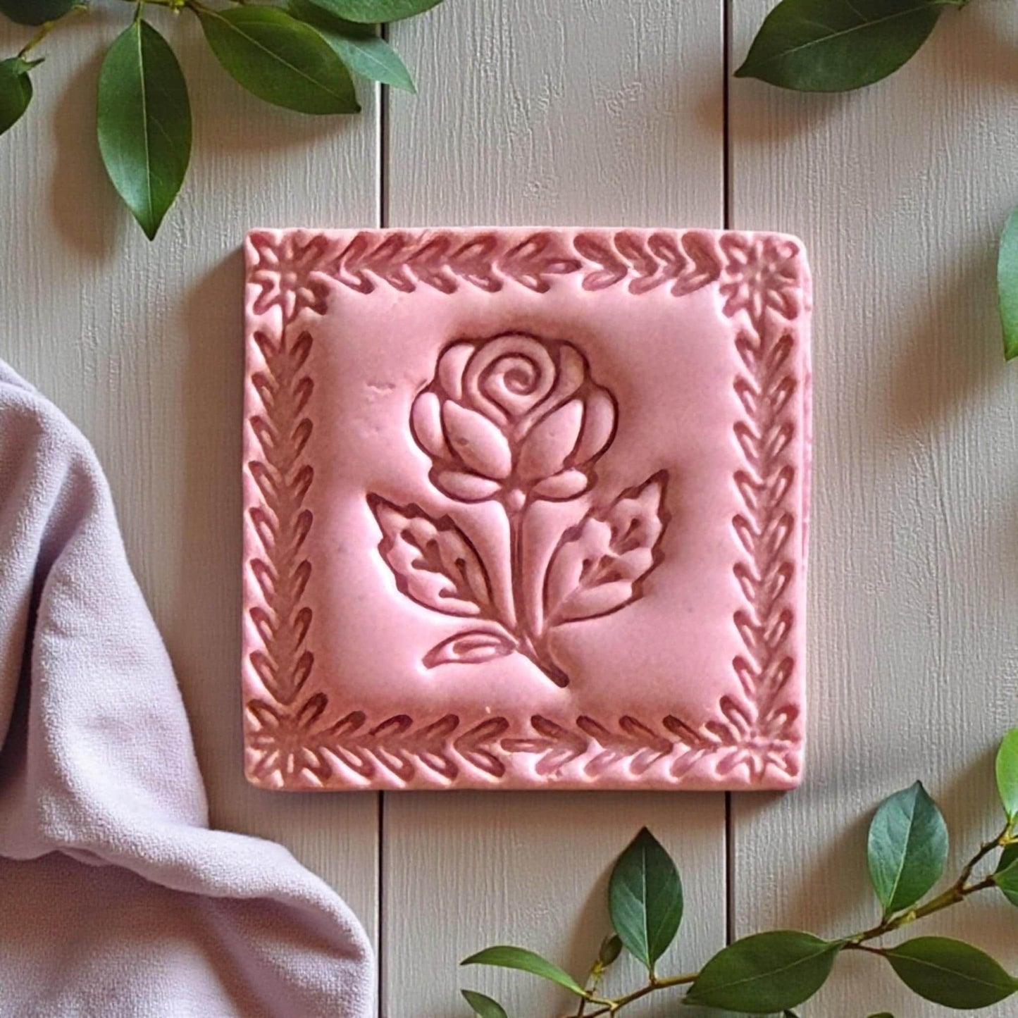 Pink clay rose square with floral border and greenery on light wood surface