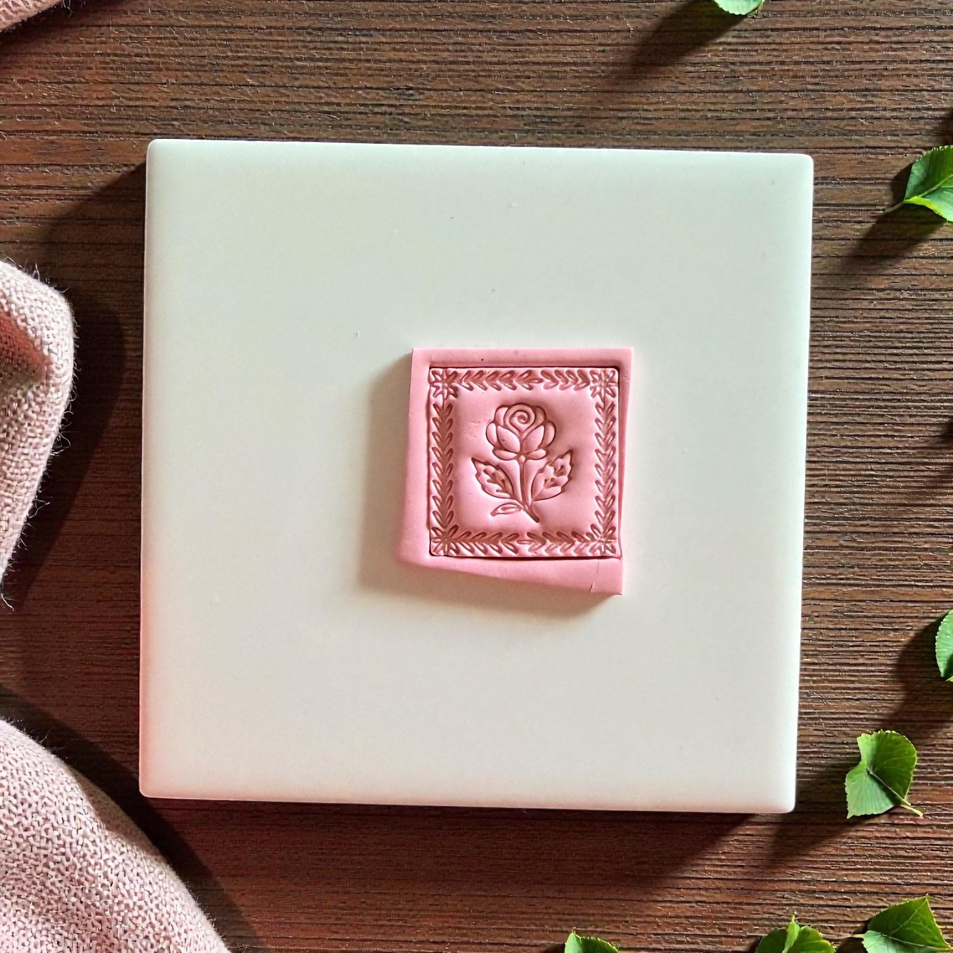 Pink clay rose square with detailed border placed on white tile background