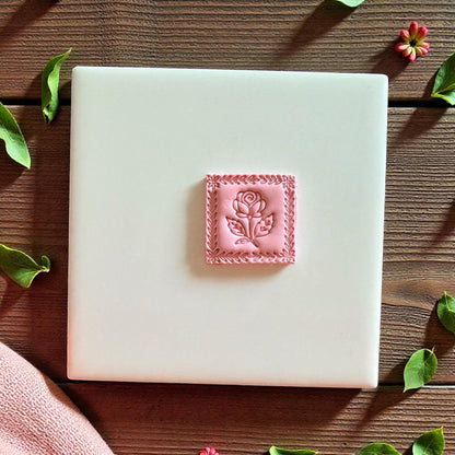 Small pink clay rose square centered on white tile with leaves around