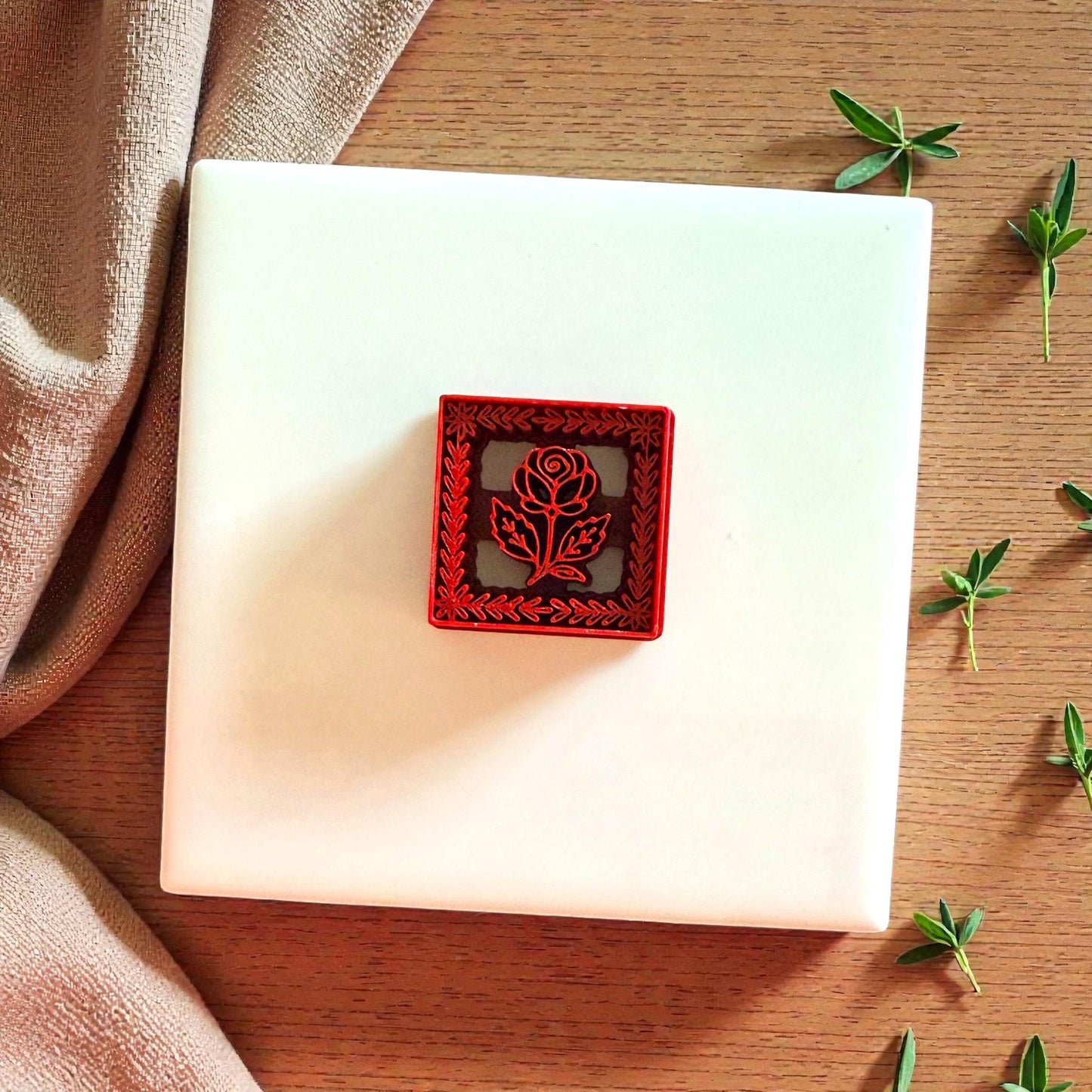 Red square floral frame cutter with rose detail on white tile and wooden background