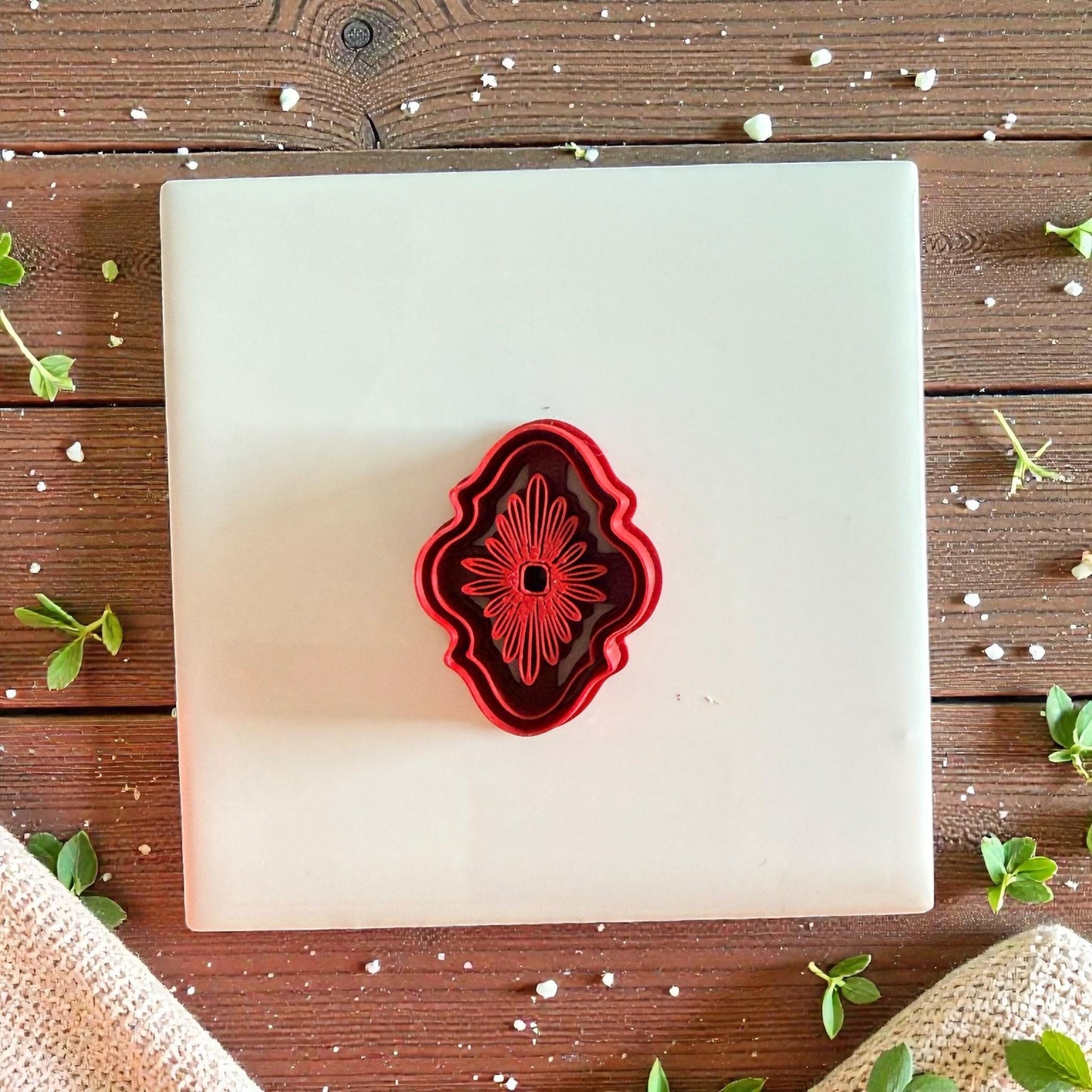 Red ornate bloom cutter centered on white tile with greenery and rustic backdrop