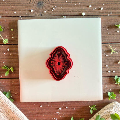Red ornate bloom cutter centered on white tile with greenery and rustic backdrop