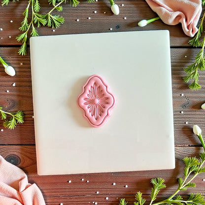 Pink ornate floral clay design centered on white tile with fabric and greenery