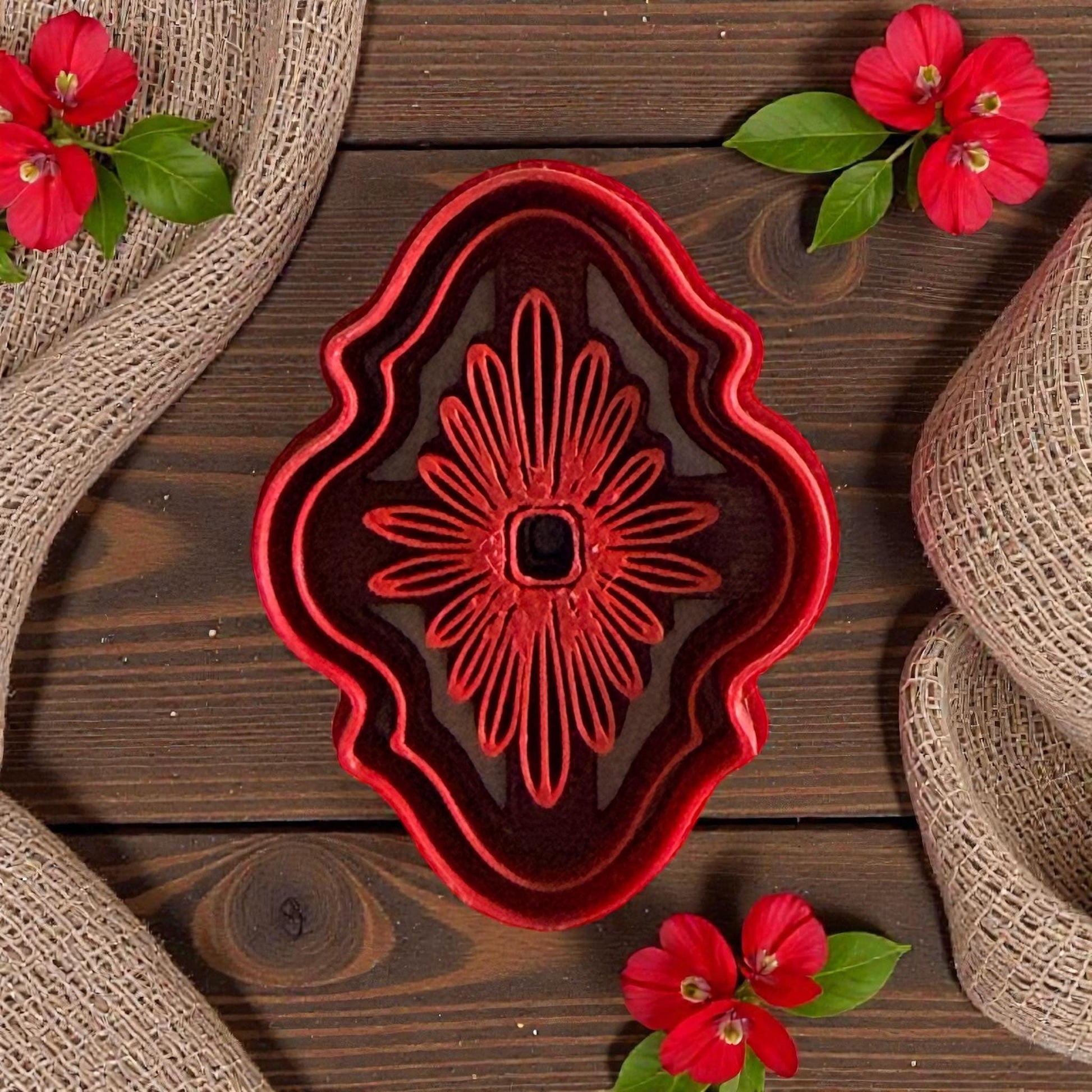 Red ornate floral polymer clay cutter with layered petal design on wood background