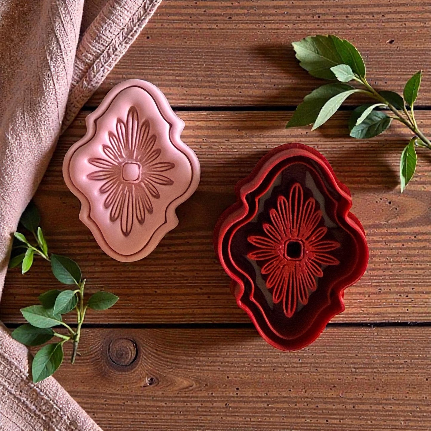 Red ornate cutter and pink clay bloom side by side on wooden background