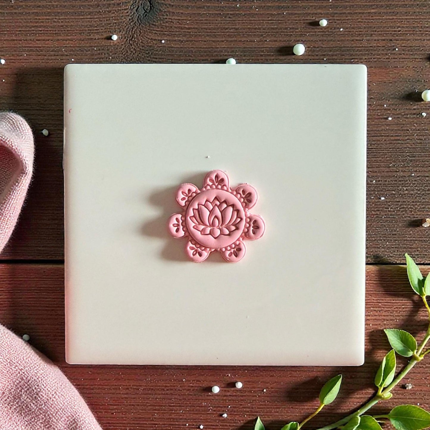 Pink lotus floral clay piece centered on white tile with rustic backdrop