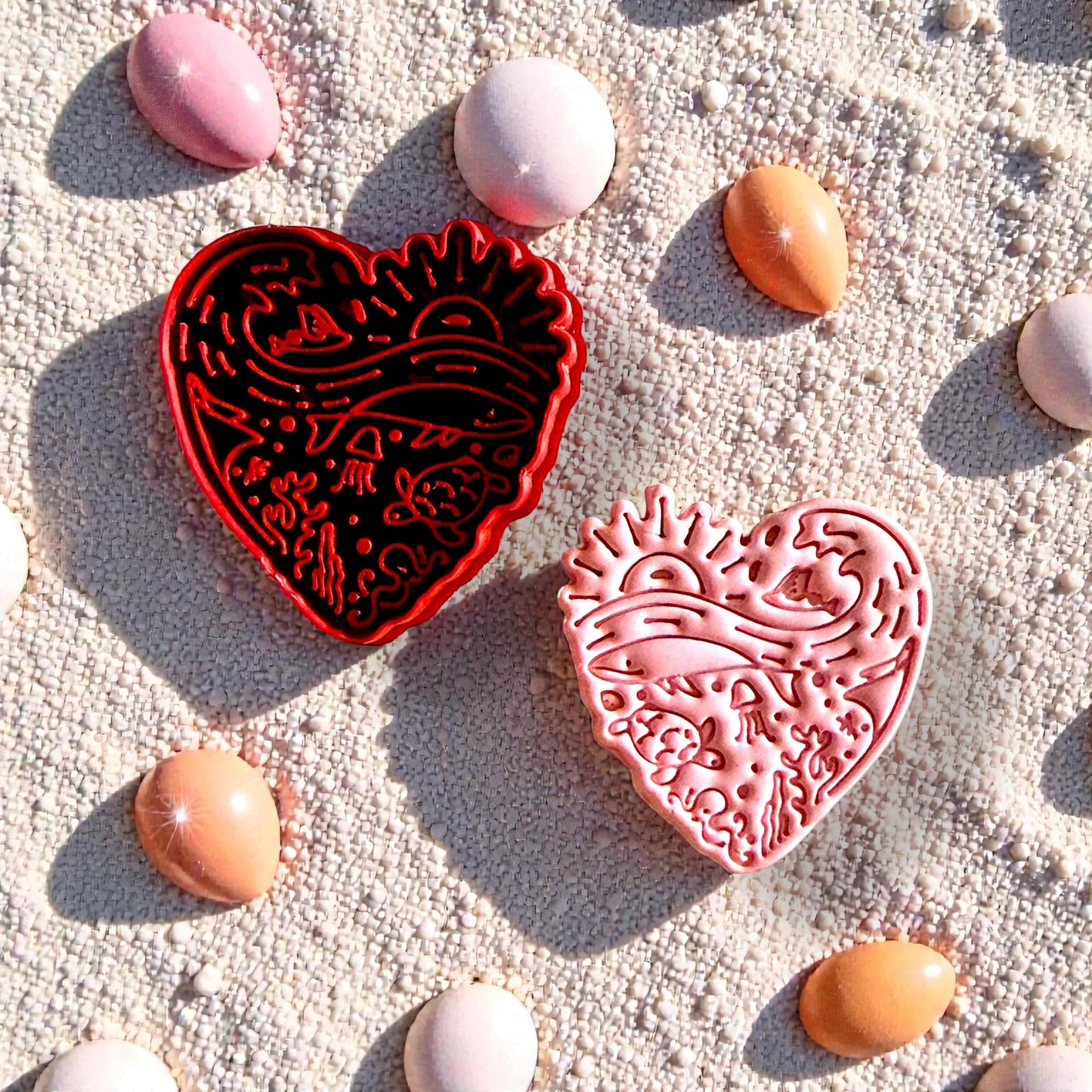 Red and pink ocean heart cutters on sand with beach pebbles