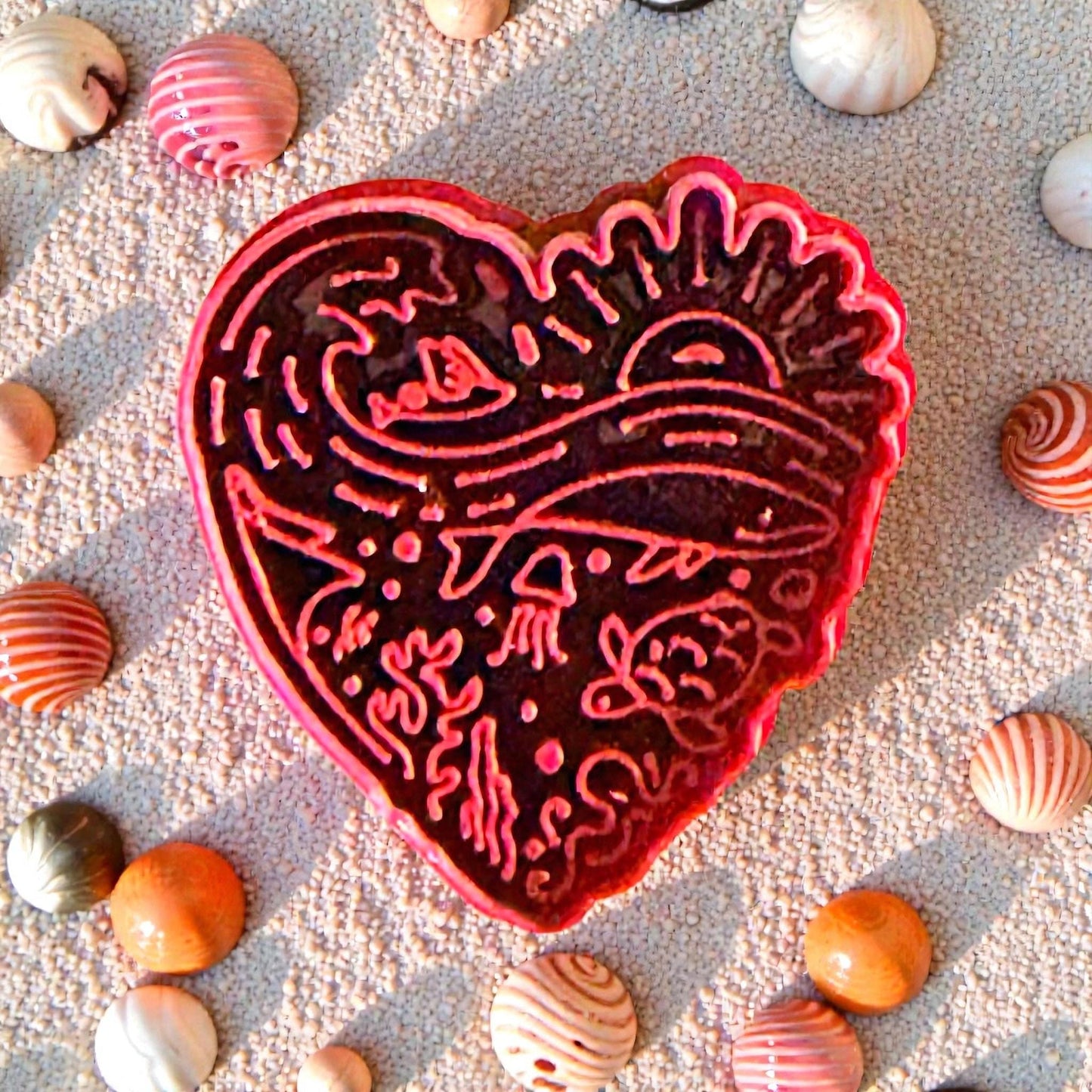 Close-up of red beach heart clay cutter with ocean design and shells