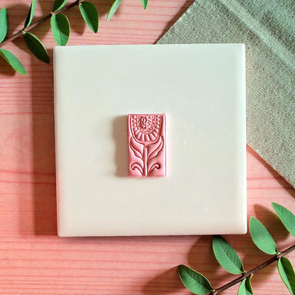 Pink rectangular floral clay piece centered on tile with leaves