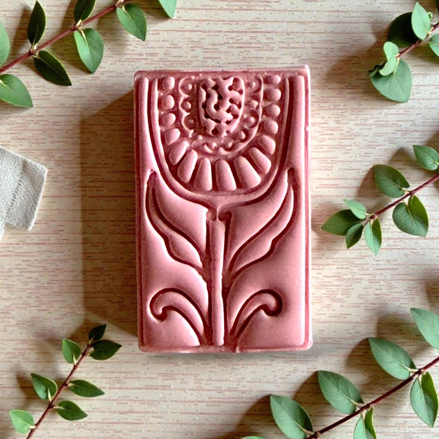 Pink folk tulip clay design with leafy details surrounded by greenery