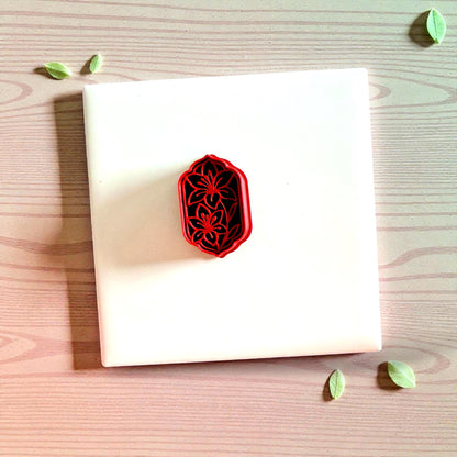 Red ornate floral cutter centered on white tile with scattered leaves