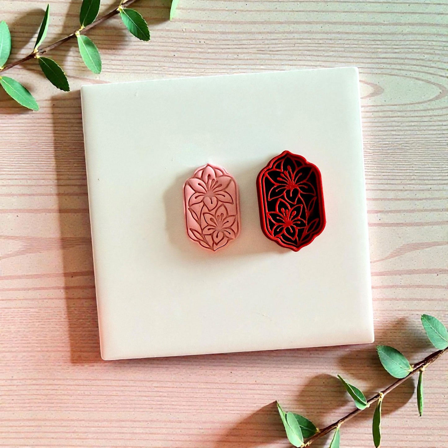 Pink clay floral impression beside red lily frame cutter on tile
