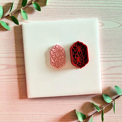 Pink clay floral impression beside red lily frame cutter on tile