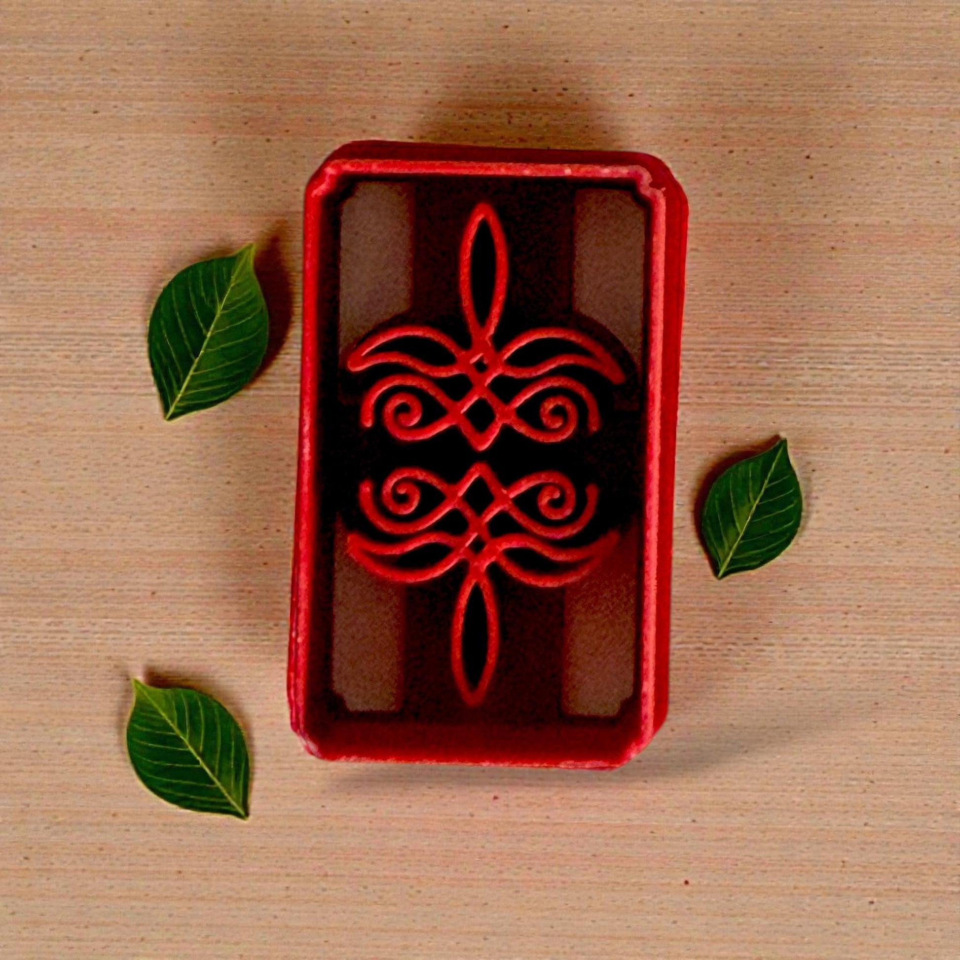 Red bootstitch cutter on textured beige cloth with greenery