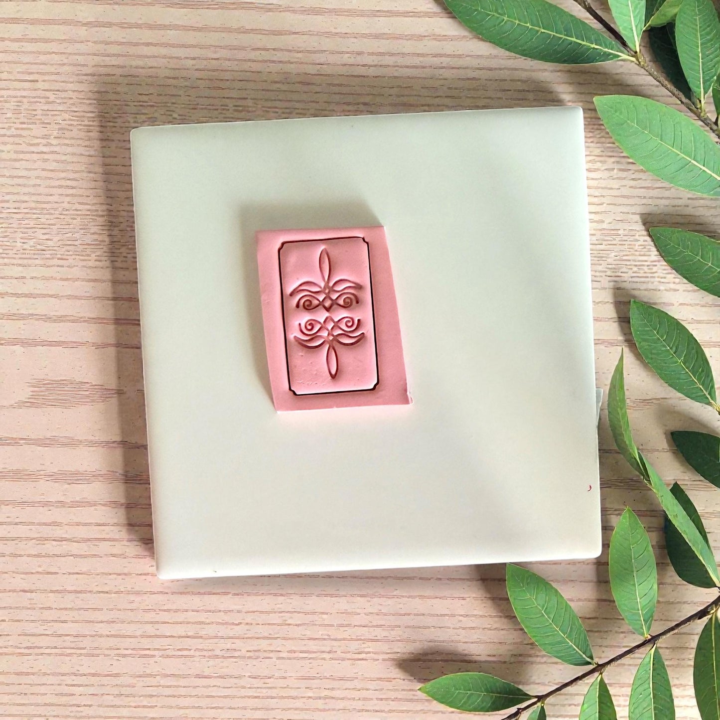 Bootstitch cutter pressed into pink clay rectangle on tile with leaves