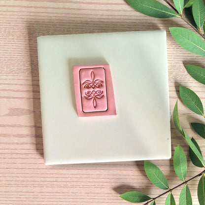 Bootstitch cutter pressed into pink clay rectangle on tile with leaves
