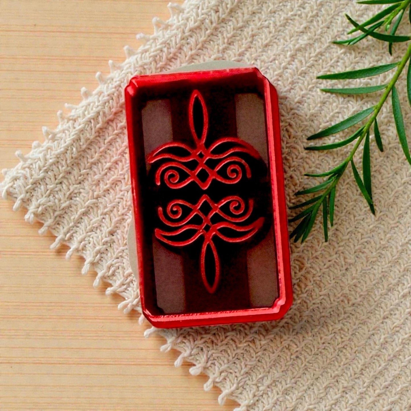 Red rectangular bootstitch polymer clay cutter with scroll design on wood surface