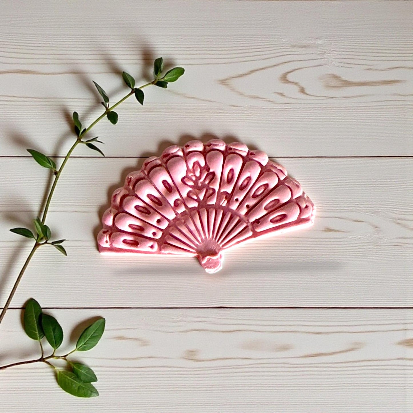 Pink clay impression of ornate floral fan design on wood background
